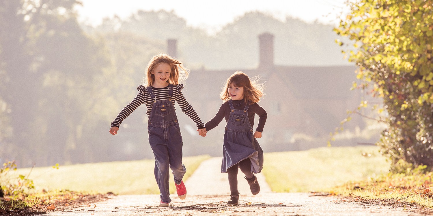 Photograph of sisters holding hands and enjoying a running race in autumn. Taken in Vachery, near Cranleigh, Surrey