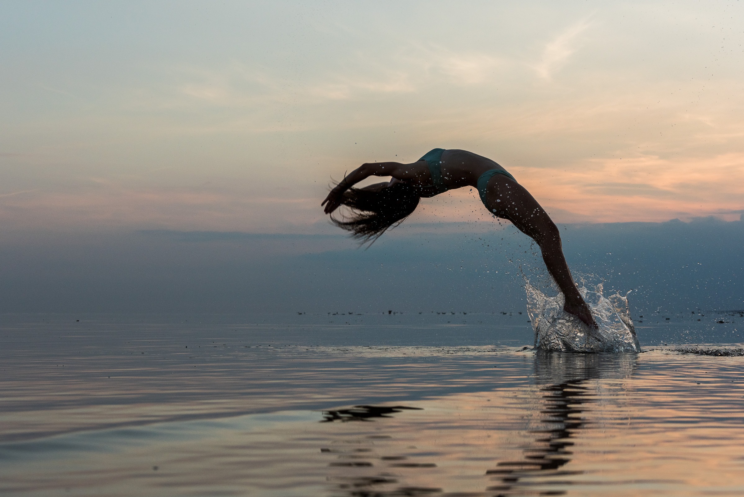 Teenage girl performing high level gymnastics in the sea at sunset